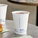 A white Solo ProPlanet paper hot cup filled with brown liquid sitting on a table next to a pastry.