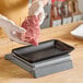 A hand holding a piece of meat over a black foam meat tray.