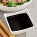 A bowl of Lee Kum Kee dark soy sauce next to a bowl of rice and chopsticks.