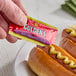 A hand holding a Gulden's Spicy Brown Mustard packet over a hot dog.