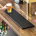A rectangular black matte surface-mount beer drip tray on a wooden bar counter.