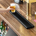 A black matte stainless steel surface-mount beer drip tray on a wooden bar counter.