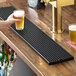 A long, rectangular black matte surface-mount beer drip tray on a wooden bar counter.