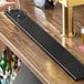 A long, black matte stainless steel beer drip tray with a built-in glass rinser, designed for mounting on a bar surface.