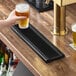 An 18 by 5 inch black matte stainless steel surface-mount beer drip tray on a bar counter.