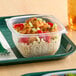 A Dart clear polypropylene square bowl filled with food on a white tray.