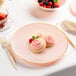 A Posh Setting pink plastic coupe plate with gold band on a table with cookies with pink frosting and berries.