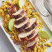 A plate of grilled chicken with rice and lime wedges.