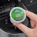 A hand holding a small green and white round container with white text that reads "Green Mountain Coffee Roasters Dark Magic"