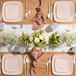 A table set with Posh Setting pink square plastic coupe plates with a gold band, napkins, and flowers.