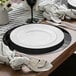 A Posh Setting black charger plate on a table with cutlery and a white napkin.