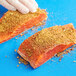 A person's hand seasoning a piece of salmon with Old Bay.