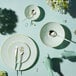 A table set with a Posh Setting turquoise plastic plate with gold silverware and flowers.