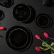 A group of Posh Setting black plastic plates with gold rims on a table with red tulips.