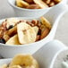 A white bowl filled with dried banana chips, nuts, and raisins.