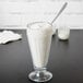 A glass of white milkshake with a straw and a spoon.