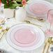 A table set with Posh Setting pink plastic coupe plates with gold cutlery and pink and gold flowers.