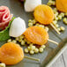 A plate with skewered dried apricots, mozzarella balls, and small pieces of salami, garnished with herbs and small round snacks.