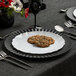 A Posh Setting white plastic plate with cookies and silverware on a table.