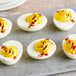 A group of deviled eggs with yellow and red toppings on a grey surface.