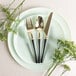 A Posh Setting gold and black plastic fork, spoon, and knife on a plate with flowers.