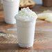 A white drink in a plastic cup with whipped cream and cookies on top.