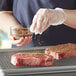 A piece of steak being seasoned with McCormick Montreal Steak Seasoning.