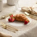 A Posh Setting clear plastic plate with strawberries, a croissant, and a gold fork.