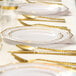 A table set with Posh Setting white plastic plates with gold bands and gold cutlery.