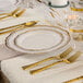 A table setting with a Posh Setting white plastic plate with gold bands and gold forks.
