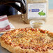 A person pouring McCormick Culinary Mediterranean Oregano onto a pizza.
