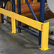 A yellow adjustable steel rack guard installed in a warehouse for protecting shelving units.