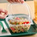 A person holding a Dart plastic container of pasta and vegetables.