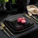 A Posh Setting black plastic plate with a gold band on a table with pink macaroons.