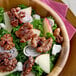 A wooden bowl filled with a salad containing raw walnut halves and pieces, kale, red onion slices, apple slices, and crumbled cheese.