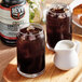 A glass of dark liquid with ice on a table in a coffee shop.