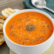 A bowl of orange soup with McCormick basil leaves on top next to a spoon and toast.