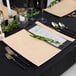 A black table set with Posh Setting beige square charger plates and silverware.