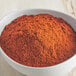 A bowl of McCormick Culinary Ground Ancho Chile Pepper powder on a wooden table.