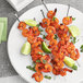 A plate of shrimp skewers with lime wedges next to a bowl of McCormick Culinary Mesquite Barbecue Seasoning.
