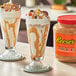 Two glasses of ice cream with peanut butter sauce and chocolate toppings on a table.