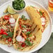 A plate of three tacos with chicken, radishes, and lime with a bowl of cilantro.