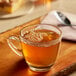 A glass cup of Bigelow green tea on a wood surface with a spoon on a plate.