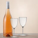 A bottle of wine and two Posh Setting plastic wine glasses on a table.