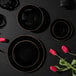 A group of Posh Setting black plastic coupe plates with gold bands on a table with red tulips.
