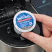 A hand holding a round blue and white Swiss Miss Milk Chocolate Hot Cocoa K-Cup Pod container.