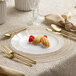 A place setting with a Posh Setting clear plastic plate with gold band, a fork, and a spoon.