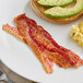 A plate with Daily's Applewood Smoked Bacon slices, avocado, and eggs on it.