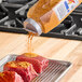 McCormick Culinary Korean BBQ Gochujang Style Seasoning being poured onto raw meat on a metal tray.