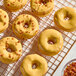 A batch of donuts with a glossy maple glaze, some topped with small crunchy bits, displayed on a cooling rack.